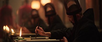 Movie still from “Mulan” (2020), directed by Niki Caro – A person wearing a hat and writing on a piece of paper; Close Up shot, High angle