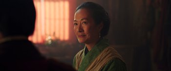 Movie still from “Mulan” (2020), directed by Niki Caro – A woman in a green dress is looking at the camera; Close Up shot, Over the shoulder angle