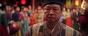 Movie still from “Mulan” (2020), directed by Niki Caro – An older man wearing a black hat and a robe; Close Up shot, Over the shoulder angle