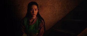 Movie still from “Mulan” (2020), directed by Niki Caro – A woman with long black hair sitting in a dark room; Medium shot, High angle