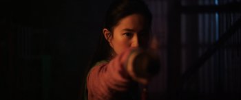 Movie still from “Mulan” (2020), directed by Niki Caro – A young woman is holding a gun in a dark room; Close Up shot, Over the shoulder angle