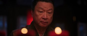 Movie still from “Mulan” (2020), directed by Niki Caro – An older asian man looking at the camera with candles in the background; Close Up shot, Low angle