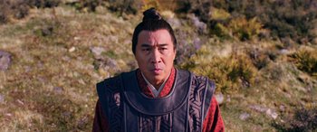 Movie still from “Mulan” (2020), directed by Niki Caro – A man in a red and black shirt and a black vest; Close Up shot, Low angle