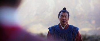 Movie still from “Mulan” (2020), directed by Niki Caro – A man with a long black hair and a blue shirt; Close Up shot, Over the shoulder angle
