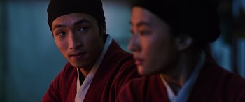 Movie still from “Mulan” (2020), directed by Niki Caro – Two men in traditional asian garb sitting next to each other; Close Up shot, Over the shoulder angle