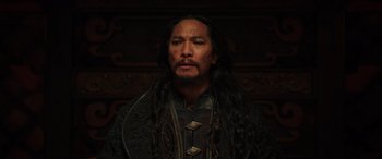 Movie still from “Mulan” (2020), directed by Niki Caro – A man with long black hair wearing a black shirt; Close Up shot, Low angle