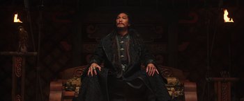 Movie still from “Mulan” (2020), directed by Niki Caro – A man sitting on top of a couch wearing a robe; Medium shot, Low angle