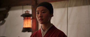 Movie still from “Mulan” (2020), directed by Niki Caro – A person wearing a black hat and a red robe; Close Up shot, Low angle