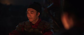 Movie still from “Mulan” (2020), directed by Niki Caro – A man wearing a black hat and a red shirt; Close Up shot, Over the shoulder angle