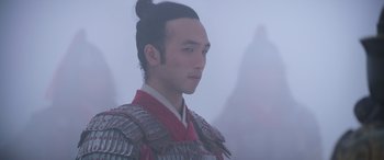 Movie still from “Mulan” (2020), directed by Niki Caro – A man in a red and black outfit standing in the fog; Close Up shot, Over the shoulder angle
