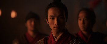 Movie still from “Mulan” (2020), directed by Niki Caro – A man in a red and black outfit is looking straight ahead; Close Up shot, Over the shoulder angle