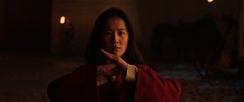 Movie still from “Mulan” (2020), directed by Niki Caro – A woman in a red robe is holding her hand up to her face; Close Up shot, Low angle