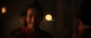Movie still from “Mulan” (2020), directed by Niki Caro – A man in a red robe smiling for the camera; Close Up shot, Over the shoulder angle