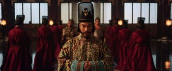 Movie still from “Mulan” (2020), directed by Niki Caro – A man wearing a hat and a robe in front of a group of people; Medium shot, Low angle