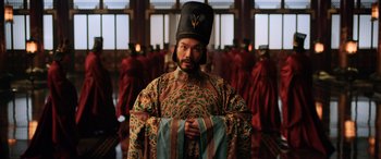 Movie still from “Mulan” (2020), directed by Niki Caro – A man wearing a hat and holding a cloth; Medium shot, Low angle