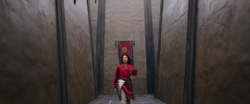Movie still from “Mulan” (2020), directed by Niki Caro – A man in a red robe is standing in a hallway; Wide shot, Low angle