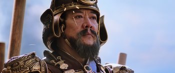 Movie still from “Mulan” (2020), directed by Niki Caro – A person with a beard wearing a helmet; Close Up shot, Low angle