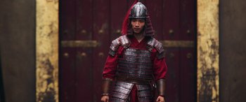Movie still from “Mulan” (2020), directed by Niki Caro – A man in a helmet and armor stands in front of a wooden door; Medium shot, Low angle