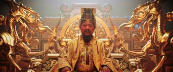 Movie still from “Mulan” (2020), directed by Niki Caro – A man sitting on a chair wearing a hat; Medium shot, Low angle