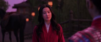 Movie still from “Mulan” (2020), directed by Niki Caro – A woman in a red robe standing in front of trees; Medium shot, Over the shoulder angle
