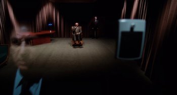 Movie still from “Mulholland Drive” (2001), directed by David Lynch – A man sitting in a chair in a dark room; Wide shot, High angle