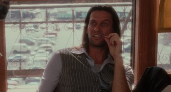 Movie still from “Mulholland Drive” (2001), directed by David Lynch – A man with long black hair is sitting in front of a window; Close Up shot, Over the shoulder angle