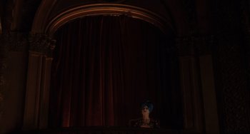 Movie still from “Mulholland Drive” (2001), directed by David Lynch – A person in a blue hat sitting in front of a curtain; Wide shot, Low angle