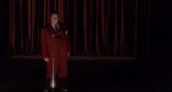 Movie still from “Mulholland Drive” (2001), directed by David Lynch – A man in a red suit standing on a stage with a microphone; Wide shot, Low angle
