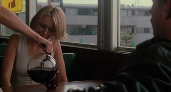 Movie still from “Mulholland Drive” (2001), directed by David Lynch – A woman sitting at a table looking at her cell phone; Medium shot, Over the shoulder angle