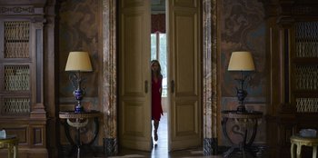 Movie still from “Murder Mystery 2” (2023), directed by Jeremy Garelick – A woman in a red dress standing in front of a door; Wide shot, Low angle
