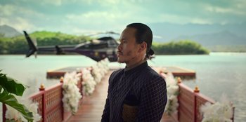 Movie still from “Murder Mystery 2” (2023), directed by Jeremy Garelick – A man standing in front of a lake and a helicopter; Medium shot, Over the shoulder angle