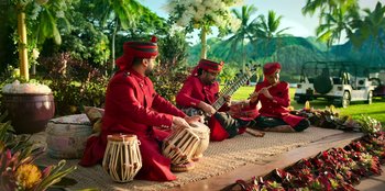 Movie still from “Murder Mystery 2” (2023), directed by Jeremy Garelick – A group of men sitting on the ground playing musical instruments; Wide shot, High angle