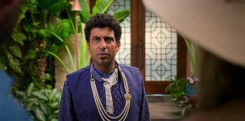 Movie still from “Murder Mystery 2” (2023), directed by Jeremy Garelick – A man in a blue shirt and a long necklace; Close Up shot, Over the shoulder angle