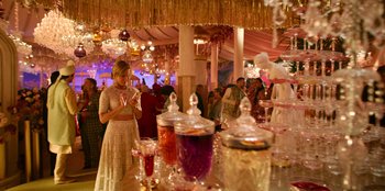 Movie still from “Murder Mystery 2” (2023), directed by Jeremy Garelick – A woman standing in front of a table filled with drinks; Wide shot, Over the shoulder angle