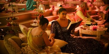 Movie still from “Murder Mystery 2” (2023), directed by Jeremy Garelick – Two women are sitting on a couch and one is reading a book; Medium shot, Over the shoulder angle