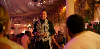 Movie still from “Murder Mystery 2” (2023), directed by Jeremy Garelick – A man in a black and white outfit is holding a cup; Medium shot, Over the shoulder angle