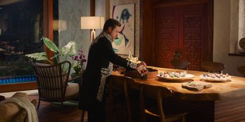 Movie still from “Murder Mystery 2” (2023), directed by Jeremy Garelick – A man sitting at a dining room table; Wide shot, High angle