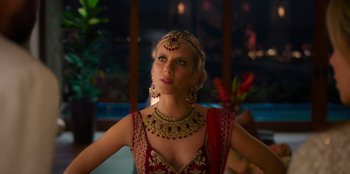 Movie still from “Murder Mystery 2” (2023), directed by Jeremy Garelick – A woman in a red and gold dress and a gold necklace; Close Up shot, Over the shoulder angle