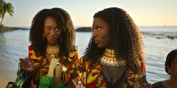 Movie still from “Murder Mystery 2” (2023), directed by Jeremy Garelick – Two black women in colorful outfits posing for a picture; Close Up shot, Over the shoulder angle