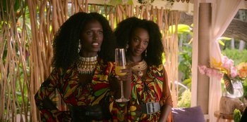 Movie still from “Murder Mystery 2” (2023), directed by Jeremy Garelick – A couple of women standing next to each other holding a glass; Medium shot, Over the shoulder angle