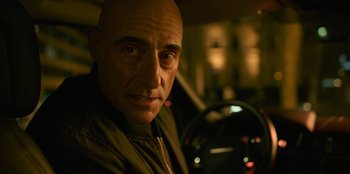 Movie still from “Murder Mystery 2” (2023), directed by Jeremy Garelick – A man with a bald head sitting in the driver's seat of a car; Close Up shot, Low angle