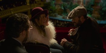 Movie still from “Murder Mystery 2” (2023), directed by Jeremy Garelick – A woman wearing a hat is sitting next to a man holding a drink; Medium shot, Over the shoulder angle