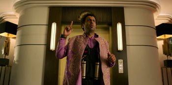 Movie still from “Murder Mystery 2” (2023), directed by Jeremy Garelick – A man in a purple suit is standing in front of an elevator; Medium shot, Low angle