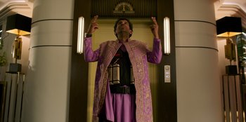 Movie still from “Murder Mystery 2” (2023), directed by Jeremy Garelick – A man wearing a purple robe and holding a gun in his hand; Medium shot, Low angle