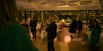 Movie still from “Murder Mystery 2” (2023), directed by Jeremy Garelick – A group of people standing in a room with a view of a city at night; Wide shot, Over the shoulder angle