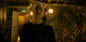 Movie still from “Murder Mystery 2” (2023), directed by Jeremy Garelick – A bald man in a black shirt is standing in a dark room; Close Up shot, Low angle