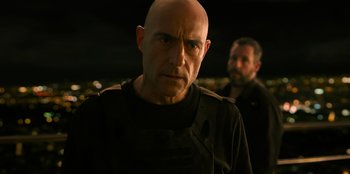 Movie still from “Murder Mystery 2” (2023), directed by Jeremy Garelick – A man with a bald head wearing a black shirt; Close Up shot, Over the shoulder angle