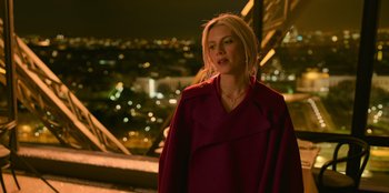 Movie still from “Murder Mystery 2” (2023), directed by Jeremy Garelick – A woman in a red coat standing in front of a window; Medium shot, Over the shoulder angle
