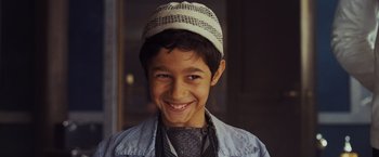 Movie still from “Murder on the Orient Express” (2017), directed by Kenneth Branagh – A young boy wearing a hat smiling for the camera; Close Up shot, High angle