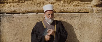 Movie still from “Murder on the Orient Express” (2017), directed by Kenneth Branagh – An older man with a beard and a white hat is holding a book; Medium shot, Low angle